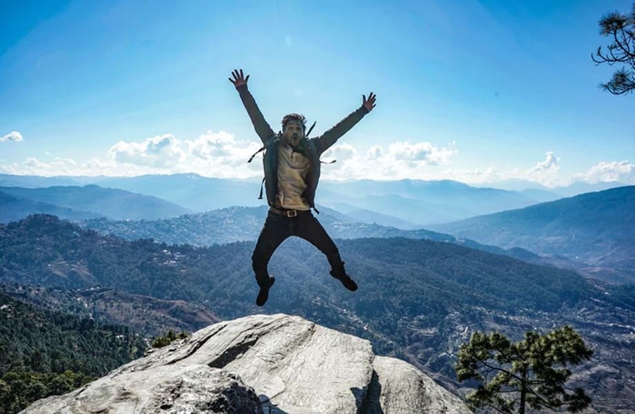 man in brown jacket jumping on mountain during daytime